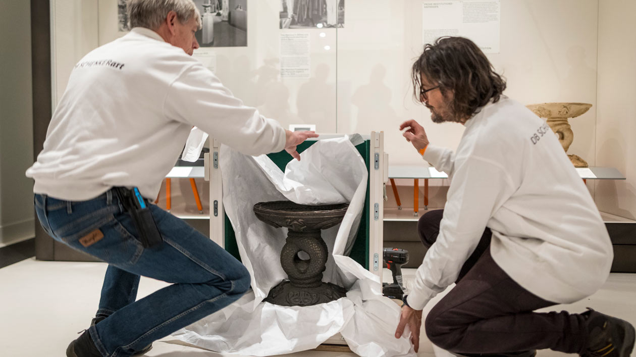 Zwei Personen verpacken ein Benin-Objekt im Ausstellungsraum