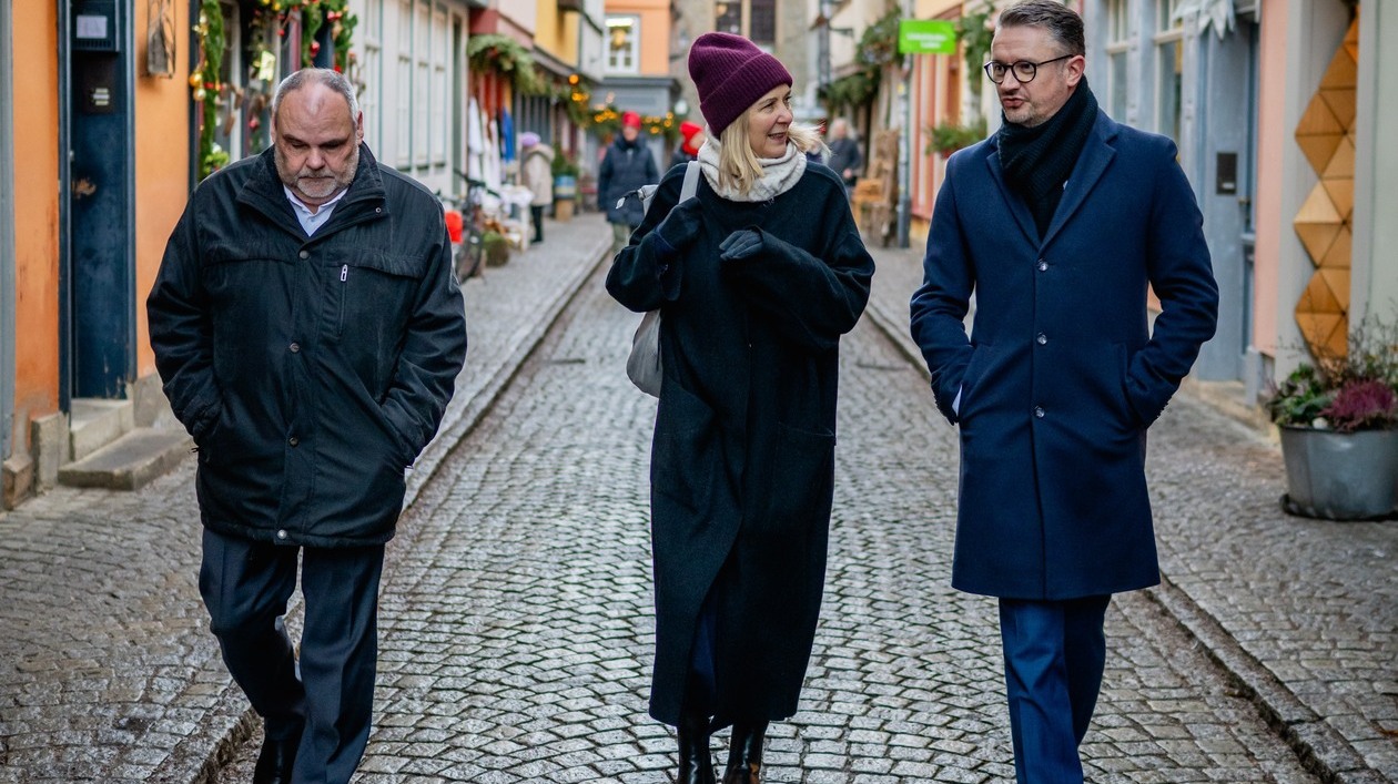 Eine Frau und zwei Männer laufen auf einer Straße entlang