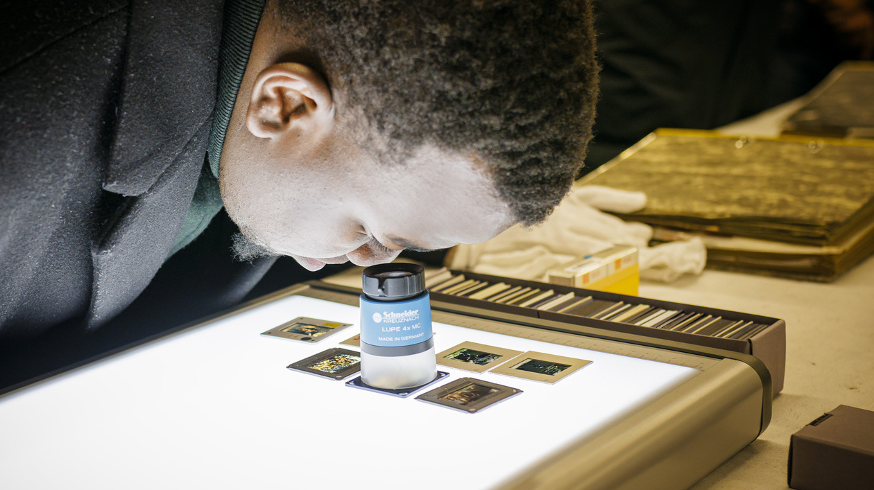 Person betrachtet Dias aus der Nuba-Fotosammlung an einem Leuchttisch.