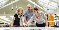 Two women and one man lean over a map